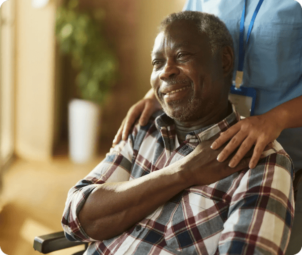 Elderly man smiling with hands on his chest, comforted by another person.