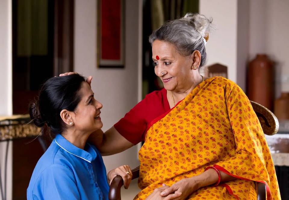 A young woman warmly embraces an elderly woman in a cozy home setting.